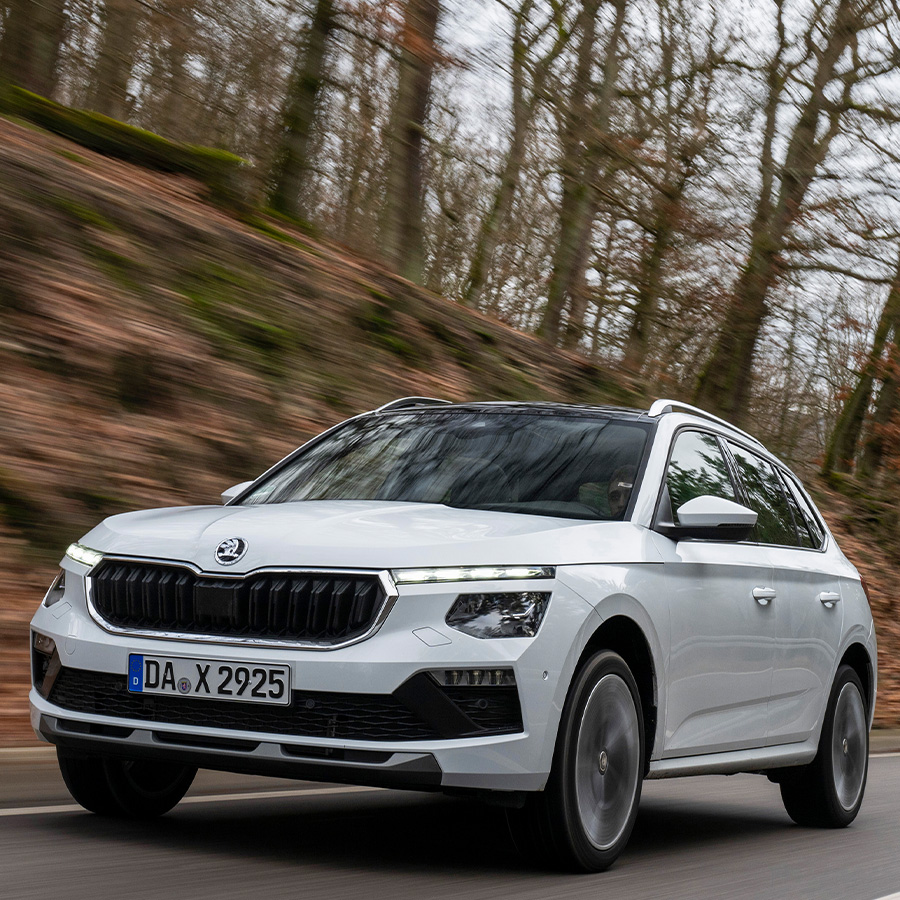 Ein wei&szlig;er Skoda Kamiq in der Dreiviertelansicht von vorne beim Fahren auf einer Landstra&szlig;e mit hohem Tempo