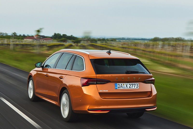 Ein orangener Skoda Combi in der Dreiviertelansicht von hinten bei der Fahrt auf einer Landstra&szlig;e mit hohem Tempo