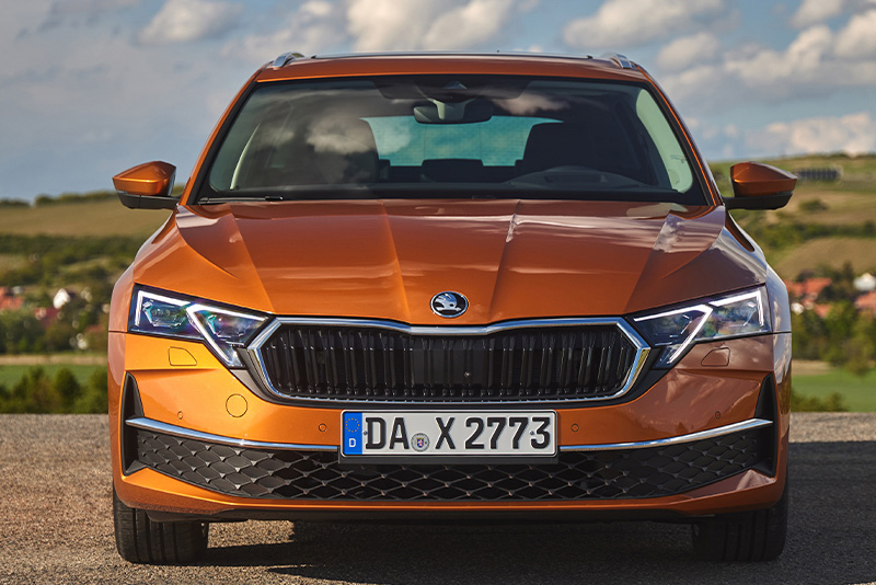 Ein orangener Skoda Octacia Combi in der Frontansicht parkend mit einer Landschaft im Hintergrund