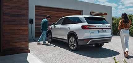 Ein Skoda Elroq in der Dreiviertelansicht von hinten beim Aufladen an einer E-Lades&auml;ule mit einem Mann und einer Frau daneben